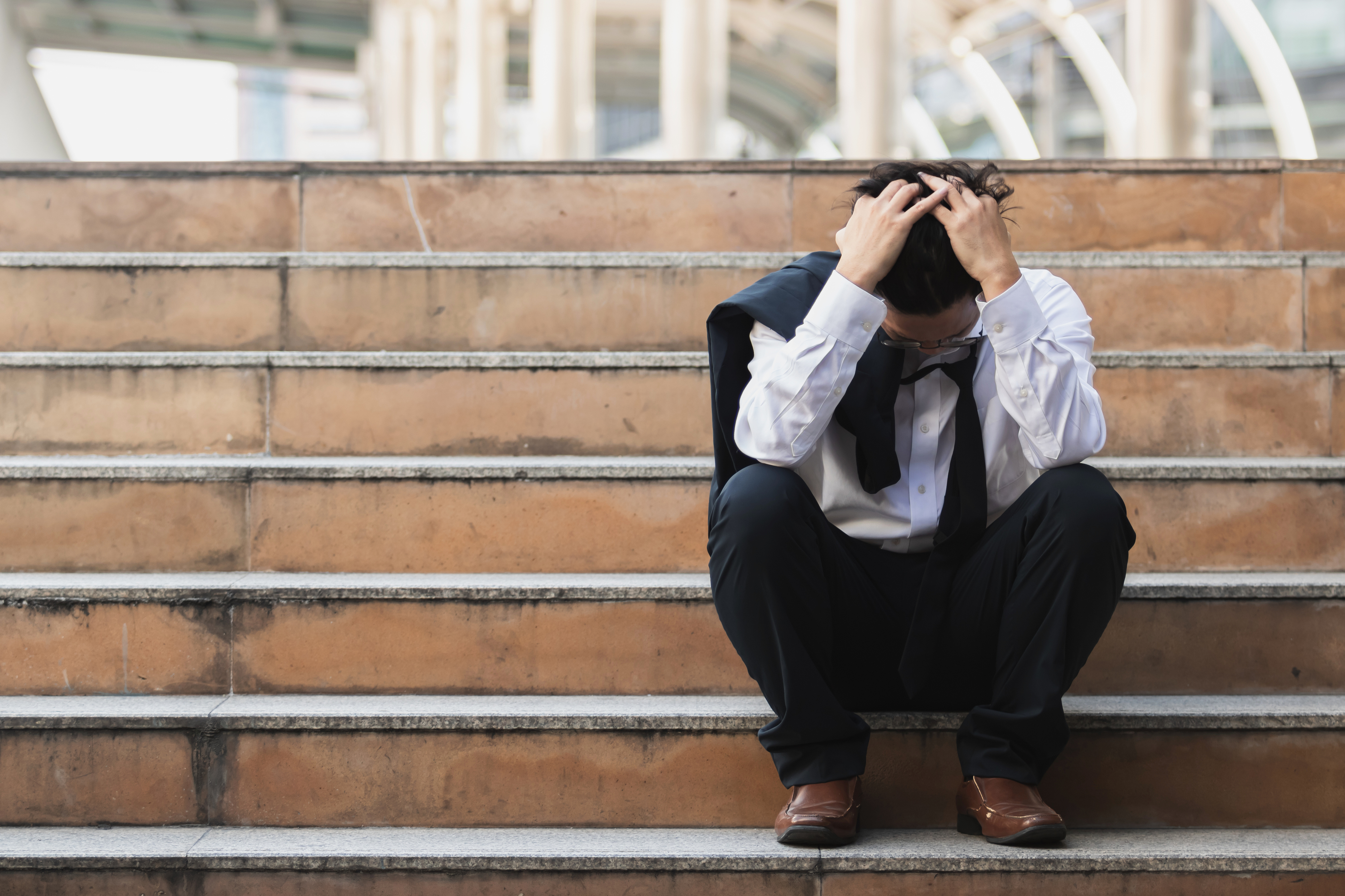 Man with his head in his hands sat on outdoor steps. 