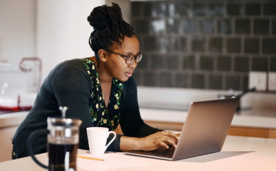 A woman working at a laptop in her kitchen.